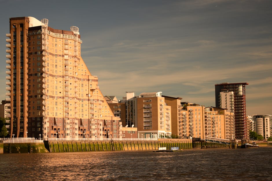 Photograph taken from across a body of water shows a row of modern residential buildings with various heights and architectural styles, some with rounded balconies and others with flat facades, under 